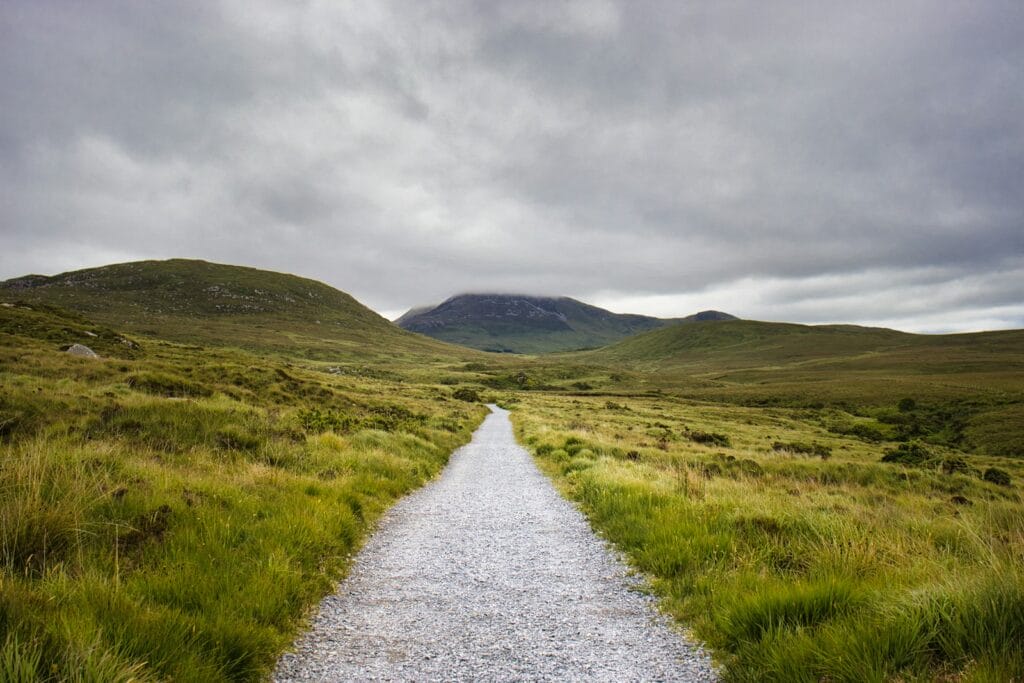 Gravel path leads through green hills under cloudy sky