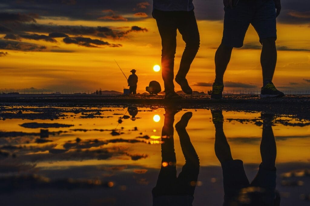 reflection of two people walking on watery field during sunset